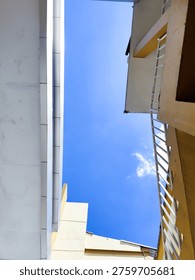 A low-angle shot of geometric building structures with white and yellow walls against a bright blue sky, showcasing minimalist architectural lines and outdoor lighting.
