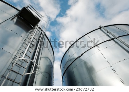 Low-angle shot of ladder and tanks refinery.
