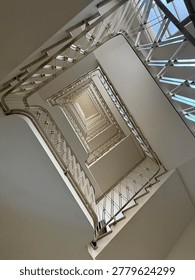 a low-angle shot looking directly up through the center of a historic, multi-story rectangular staircase