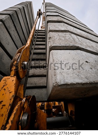 A low-angle shot looking up at massive stacked concrete blocks acting as counterweights on a heavy-duty construction crane, with steel cables and weathered yellow metal.