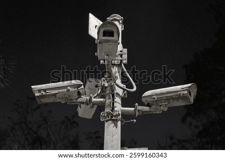 Low-angle shot of multiple old security cameras on a metal pole against a dark sky. The cameras are weathered, creating a dramatic, dystopian feel.