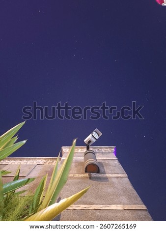 A low-angle shot of a security camera mounted on a building against a dark, starry night sky.