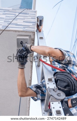 Low-angle shot of a security technician installing exterior surveillance.