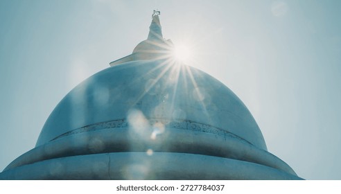 Low-angle sunlit view of massive light blue dome structure of Japanese Peace Pagoda at Rumassala. Dramatic architectural perspective with clear sky and lens flare effect highlighting monument.