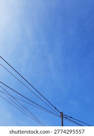 A low-angle texture photograph showing multiple electric utility wires and a utility pole against a partly cloudy blue sky