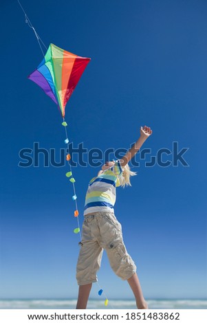 Imagen vertical de ángulo bajo de un niño saltando y llegando a una cometa bajo el cielo azul.