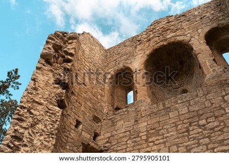 Low-angle view of ancient stone castle ruins with arched openings, rough masonry texture, and bright blue sky with soft clouds.