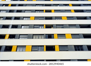 Low-angle view of apartment building combining horizontal balcony bands with recurring yellow accent panels. Conveys architectural rhythm, systematic facade composition, and contemporary visual identity.