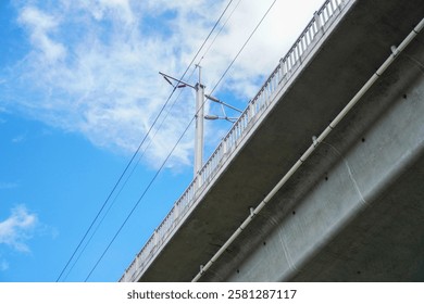 A low-angle view of a bridge's underside against a bright blue sky with fluffy clouds. Underneath the Bridge's Concrete Structure on a Sunny Day