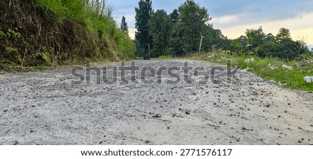A low-angle view of a bumpy, gravelly dirt road leading into a natural environment with lush green trees and foliage.