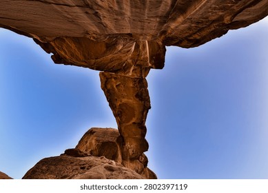 Low-angle view of Burdah Rock Bridge in Wadi Rum, Jordan. The massive natural sandstone arch rises dramatically against a clear blue sky, highlighting the unique geological formations of the UNESCO World Heritage desert landscape.