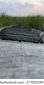 A low-angle view captures the rustic, textured planks of an old, abandoned wooden boat, hinting at forgotten journeys amidst lush green marshland under a gentle sky.
