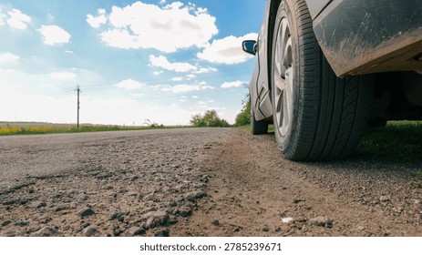 A low-angle view captures the side of a vehicle parked on a gravel shoulder next to an asphalt road, with a vast sky overhead