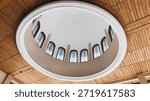 Low-angle view of a circular architectural dome with stained glass windows set into a wooden plank ceiling. Modern interior design with elegant lighting and symmetry. High quality.