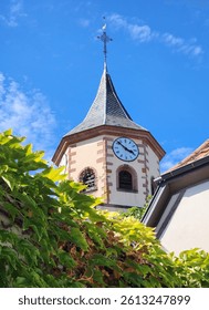 Low-angle view of a clock tower in a quaint European town seen from below an ivy covered wall