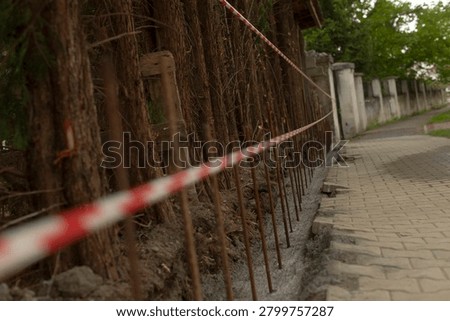 Low-angle view of a construction boundary beside a paved sidewalk showing vertical rusted steel rebars set into fresh concrete and marked off