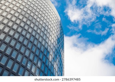 Low-angle view of a contemporary skyscraper facade with a geometric grid pattern reflecting the sky. Concept of modern architecture, business growth, and urban development.