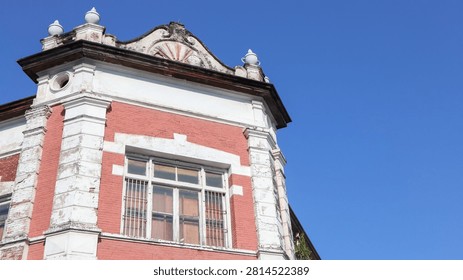Low-angle view of the corner of a historic red brick building showing intricate architectural details and ornamentation against a clear blue sky.