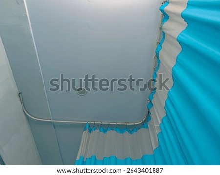 A low-angle view of a corner in a room, showcasing light blue and white striped curtains hanging from a curved track installed on the ceiling.  The ceiling i...