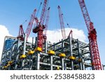 Low-angle view of cranes and steel structures of building construction with a blue sky background.