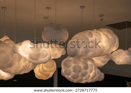 A low-angle view of a creative lighting installation featuring a cluster of cloud-shaped pendant lamps suspended from the ceiling, glowing with soft warm light to create a dreamy atmosphere.
