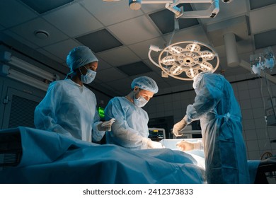 Low-angle view of diverse cooperating team of doctors, surgeons and African-American nurse processing surgical operation in operating room modern hospital emergency department. Concept of surgery.