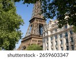 A low-angle view of the Eiffel Tower partially obscured by lush green trees, juxtaposed with a classic Parisian building.  The image evokes a serene, romantic mood, ideal for travel brochures
