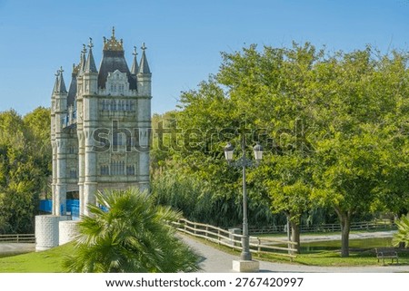 Low-angle view of the facade. Replica of the Tower of London bridge in a park in Torrejón de Ardoz, with a path crossing the lawn over a lake 