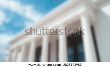 A low-angle view of a grand classical building featuring imposing columns against a bright blue sky with scattered clouds.