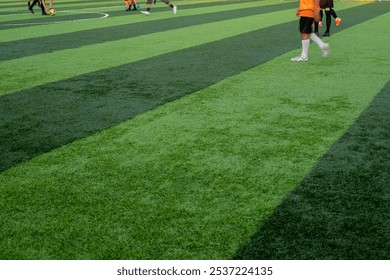 A low-angle view of a green soccer field with players' legs in action during a game. The vibrant artificial turf highlights the energy and motion of the match - Powered by Shutterstock