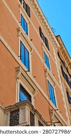 A low-angle view of a historic building facade, showcasing its warm-toned walls, multiple windows, and intricate decorative elements under a clear blue sky.