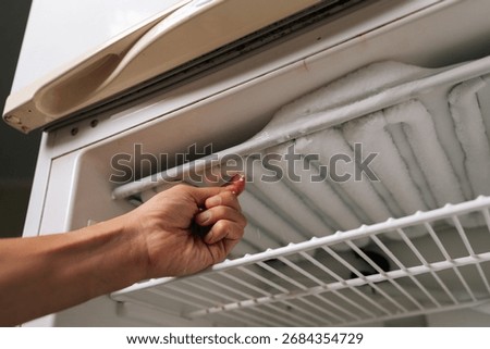 Low-angle view of housekeeper removing ice buildup from freezer compartment of refrigerator, highlighting need for regular defrosting and cleaning to maintain optimal appliance performance.