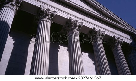 A low-angle view of imposing classical columns supporting a building facade against a clear blue sky.