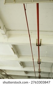 A low-angle view of an industrial ceiling featuring exposed red fire sprinkler pipes, white concrete support beams, and electrical conduit wiring.