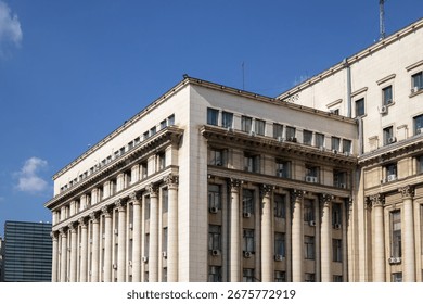 A low-angle view of a large, imposing neoclassical building featuring a prominent row of columns and many windows