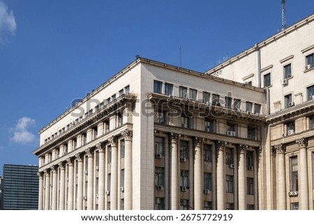 A low-angle view of a large, imposing neoclassical building featuring a prominent row of columns and many windows
