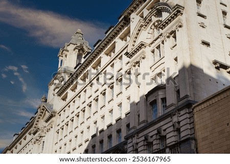 A low-angle view of a large, white stone building with numerous windows, intricate detailing, and a section of a brick building to the right.  in Manchester, UK.