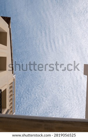 A low-angle view looking straight up along the corner of a cream-coloured apartment building in Pego, Spain, set against a dramatic sky filled with dense, textured altocumulus 