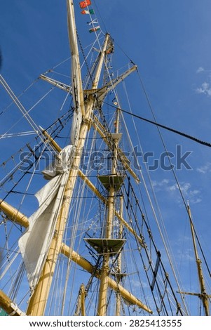Low-angle view looking up at tall sailing ship masts, spars, ropes and rigging against a clear blue sky.