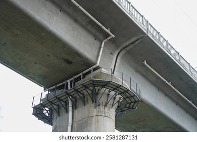 Low-angle view of a massive concrete highway bridge, showcasing its robust infrastructure and engineering. The image focuses on the bridge's underside, with visible support structures and details.