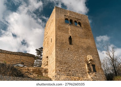 Low-angle view of a medieval stone tower and fortress ruins under blue sky and clouds, showing historic masonry and old architecture