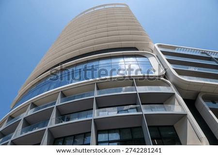 Low-angle view of Mercury Tower in St Julian, Malta, showing curved modern facade, glass balconies and reflective windows against a clear blue sky.