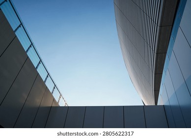 A low-angle view of modern architectural structures with sleek panels and glass railings against a clear blue sky, showcasing minimalist design.