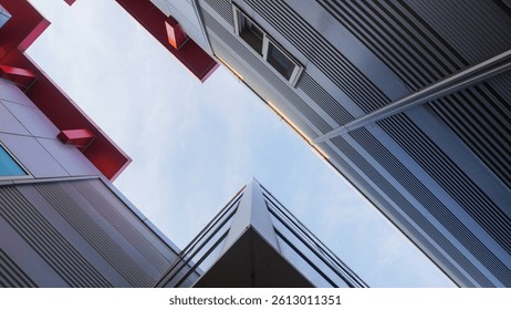 Low-angle view of modern architecture with sharp angles, red accents, and glass windows against a bright, slightly cloudy sky.