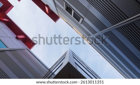 Low-angle view of modern architecture with sharp angles, red accents, and glass windows against a bright, slightly cloudy sky.