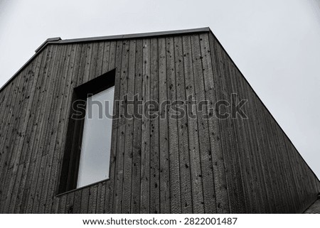 Low-angle view of a modern building clad in black Shou Sugi Ban timber, featuring vertical charred boards, a reflective window, geometric lines, and sky copy space
