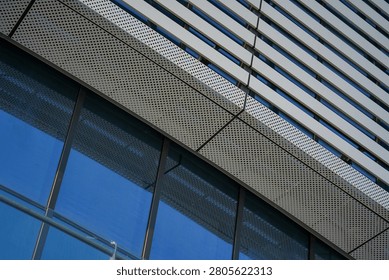 A low-angle view of a modern building facade combining perforated metal panels, glass windows, and linear slats, showcasing sleek architectural details.