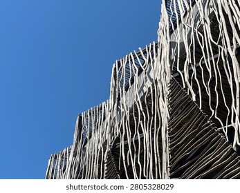 A low-angle view of a modern building featuring a wooden stick facade against a clear blue sky. Ideal for architectural design projects or sustainable housing blogs.