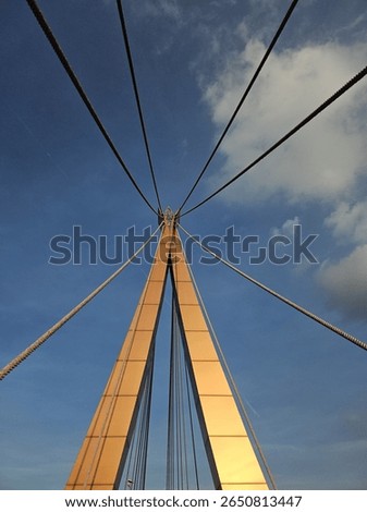 A low-angle view of a modern cable-stayed bridge against a blue sky. The cables and structure form a symmetrical pattern. Captured in Thailand on June 16, 2025.