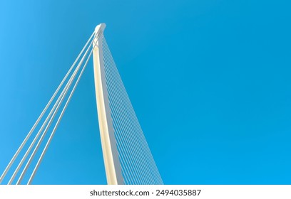 Low-angle view of a modern suspension bridge against a clear blue sky, emphasizing structural engineering, sleek design, and urban architecture. - Powered by Shutterstock